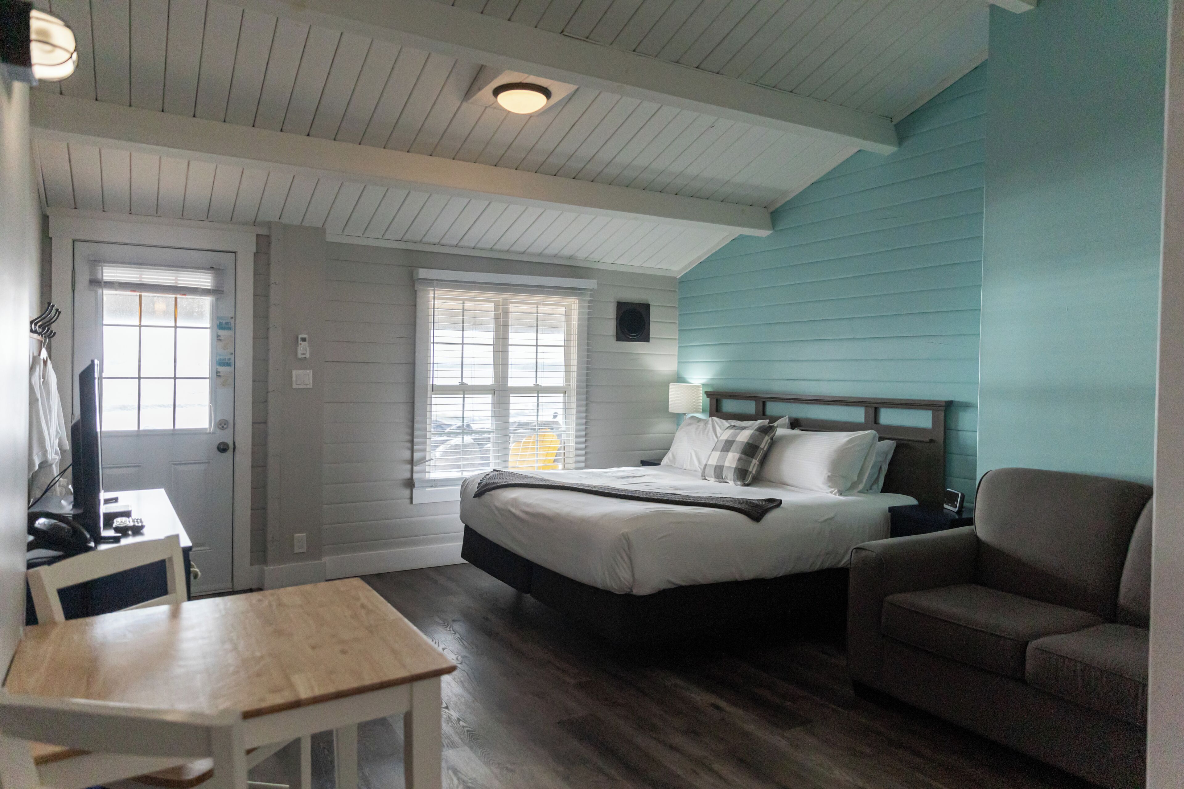 Un dormitorio con cama, una silla, una mesa y un ventanal.