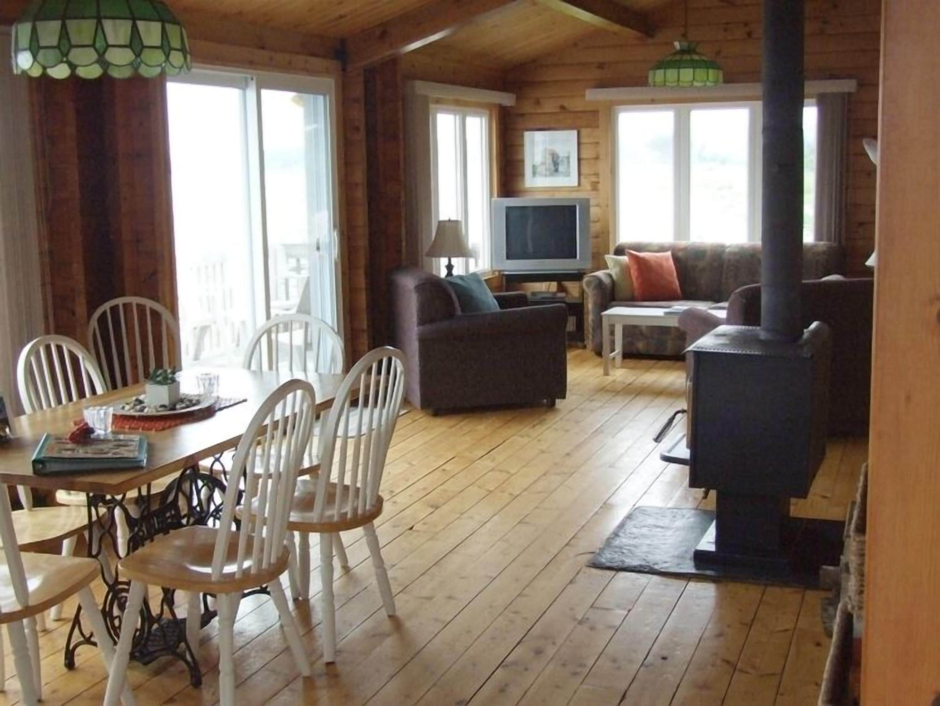 Un intérieur de chalet chaleureux comprenant un coin repas, un canapé, un téléviseur et un poêle à bois.
