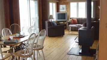 Un intérieur de chalet chaleureux comprenant un coin repas, un canapé, un téléviseur et un poêle à bois.