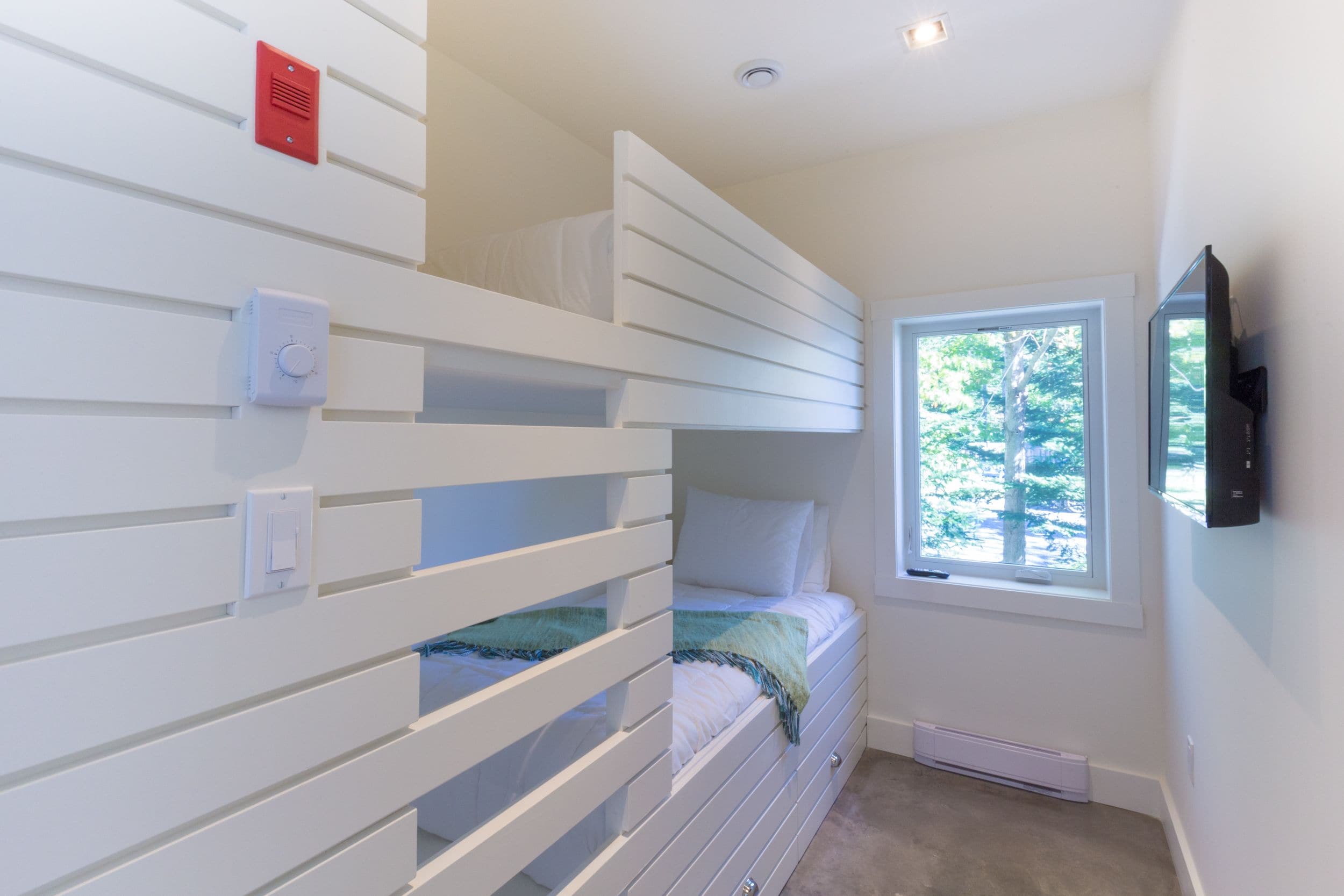 A bedroom with bunk beds, a window, a thermostat, and a mounted TV.