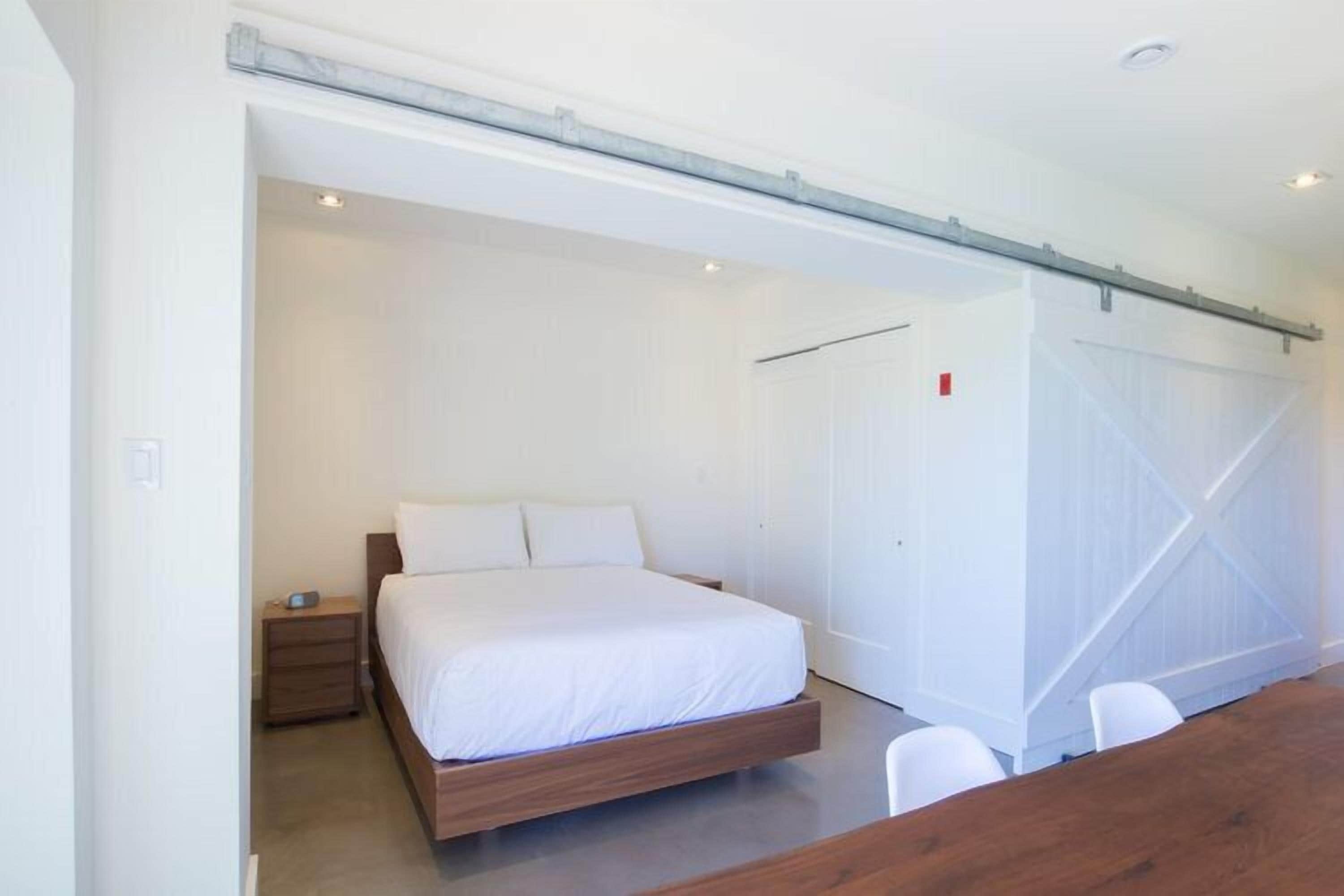 A modern bedroom with a large bed, a wooden nightstand, and a white wardrobe.