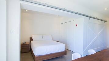 A modern bedroom with a large bed, a wooden nightstand, and a white wardrobe.