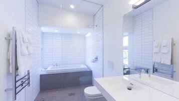 A modern bathroom with white tiles, a bathtub, a toilet, and a large mirror.