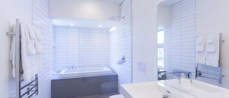 A modern bathroom with white tiles, a bathtub, a toilet, and a large mirror.