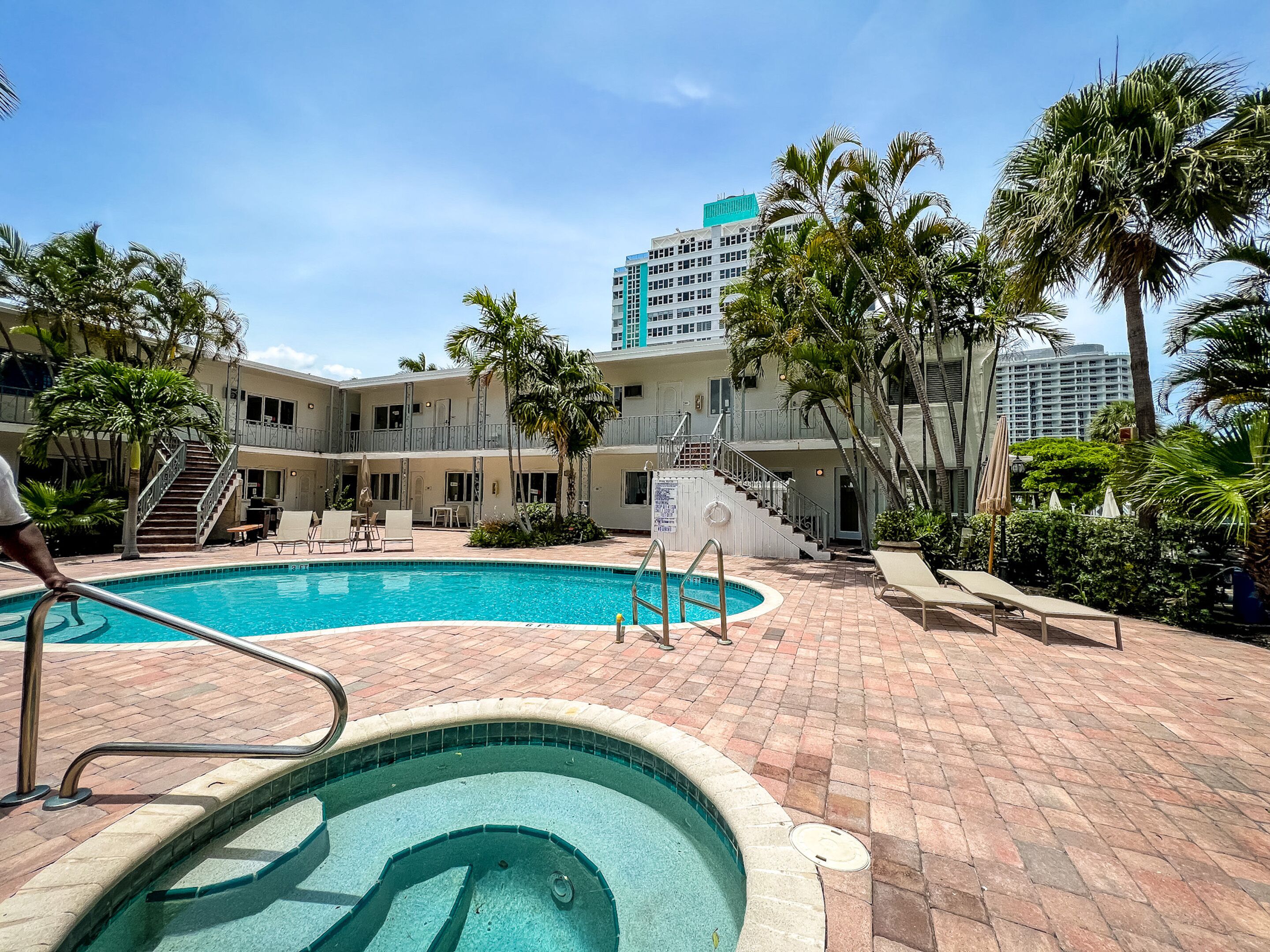 A pool area with a hot tub, lounge chairs, and palm trees.