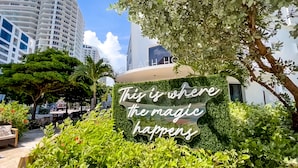 A sign with the text "This is where the magic happens" surrounded by lush greenery. - North Beach Hotel (Fort Lauderdale)