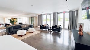 A spacious living area with a large sofa, ottoman, and armchairs, a dining area, and a kitchen in the background. - North Beach Hotel (Fort Lauderdale)
