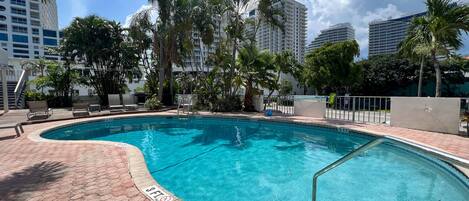 A swimming pool with a 3 FT depth marker, surrounded by palm trees and modern buildings.