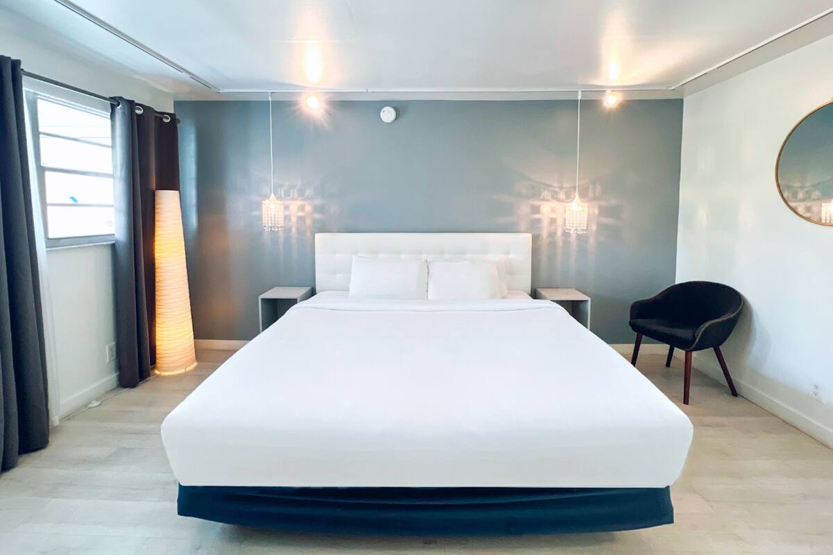 Moderni hotellihuone, jossa on suuri sänky, yöpöydät, tuoli ja kattokruunu.
