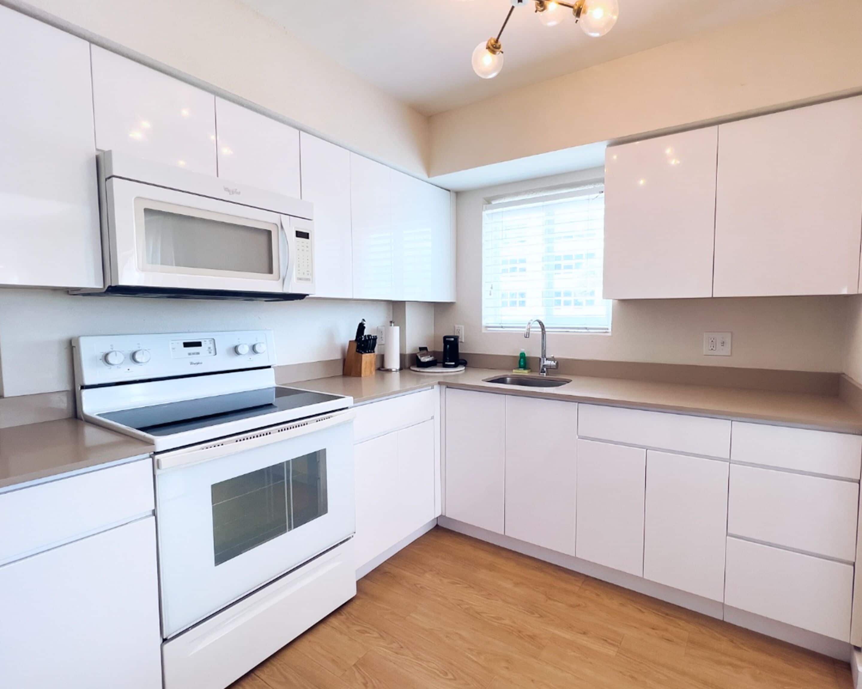 A modern kitchen with white cabinetry, a built-in microwave, a stove, and a sink.