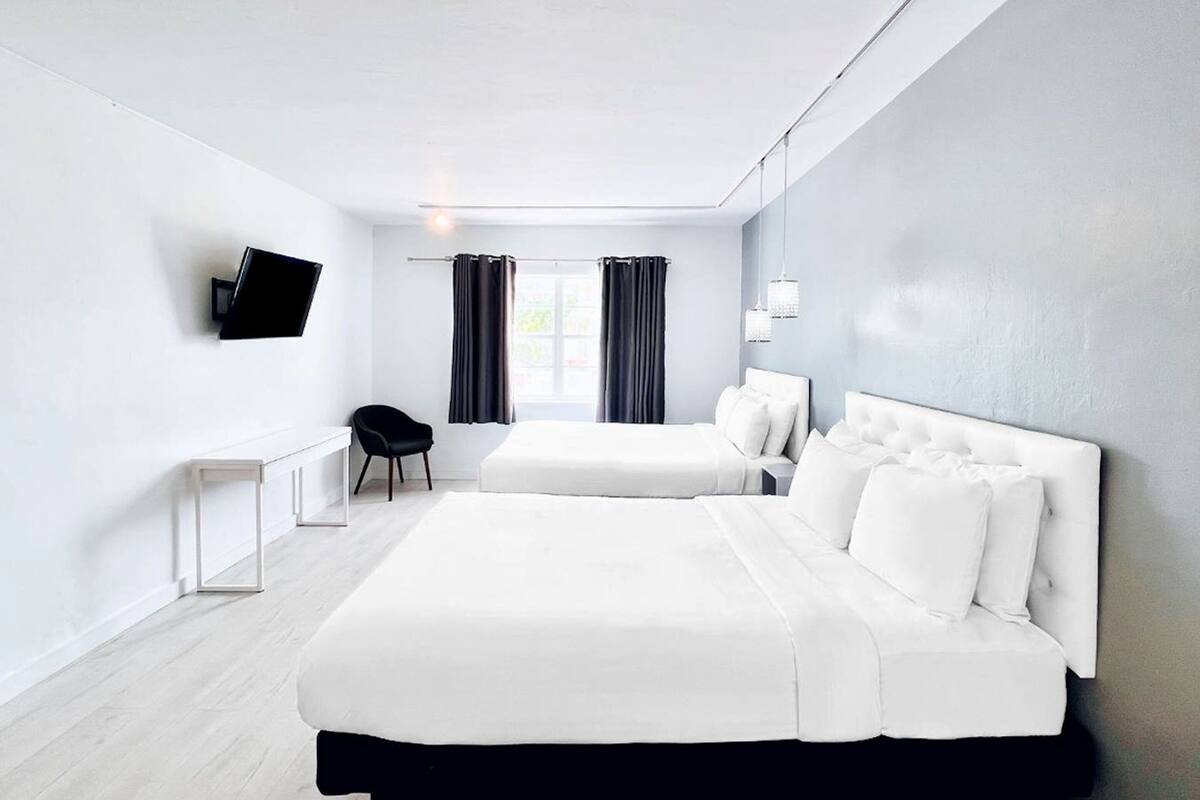 Moderni hotellihuone, jossa on suuri sänky, pieni työpöytä, tuoli ja seinälle asennettu televisio.