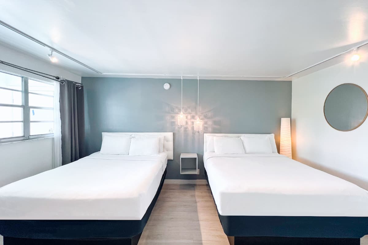 Moderni hotellihuone, jossa on kaksi erillistä sänkyä, suuri ikkuna ja koristeellinen kattokruunu.