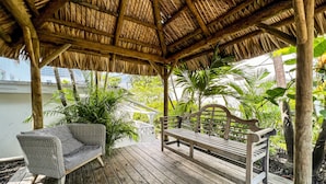A wooden deck with a thatched roof, wicker furniture, and lush greenery. - North Beach Hotel (Fort Lauderdale)