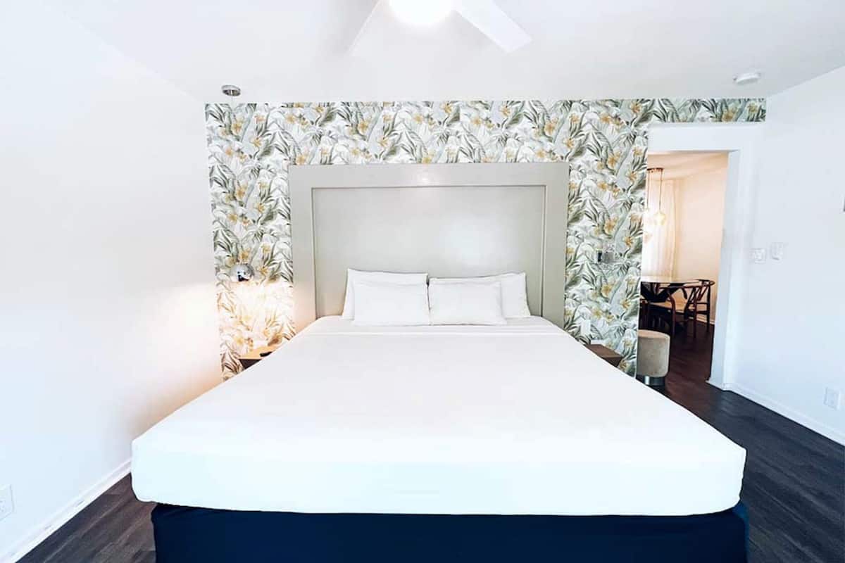 Moderni hotellihuone, jossa on suuri sänky, kattotuuletin ja kukallinen tapetti.