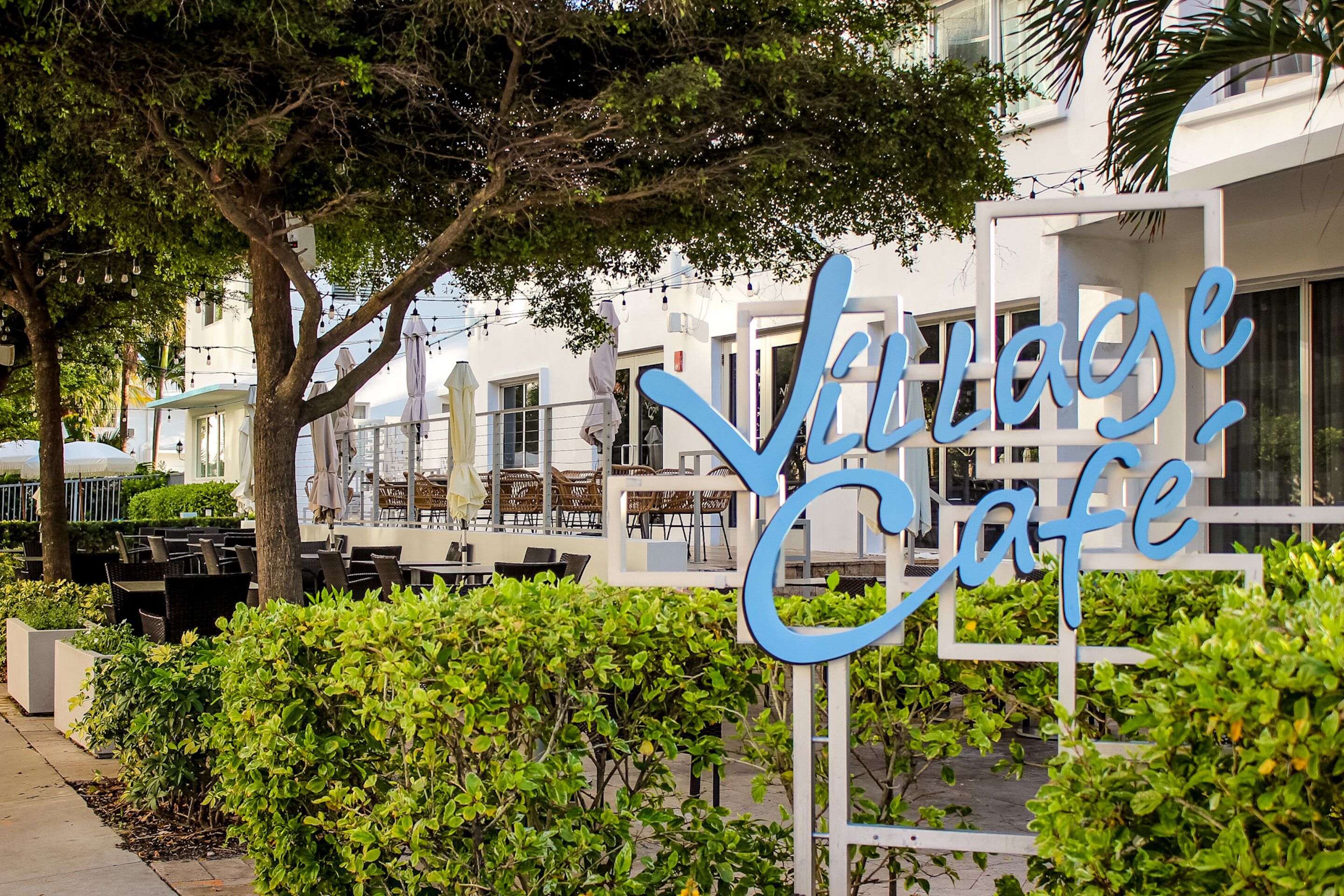 A sign for 'Villa Cafe' with outdoor seating and a white building in the background.