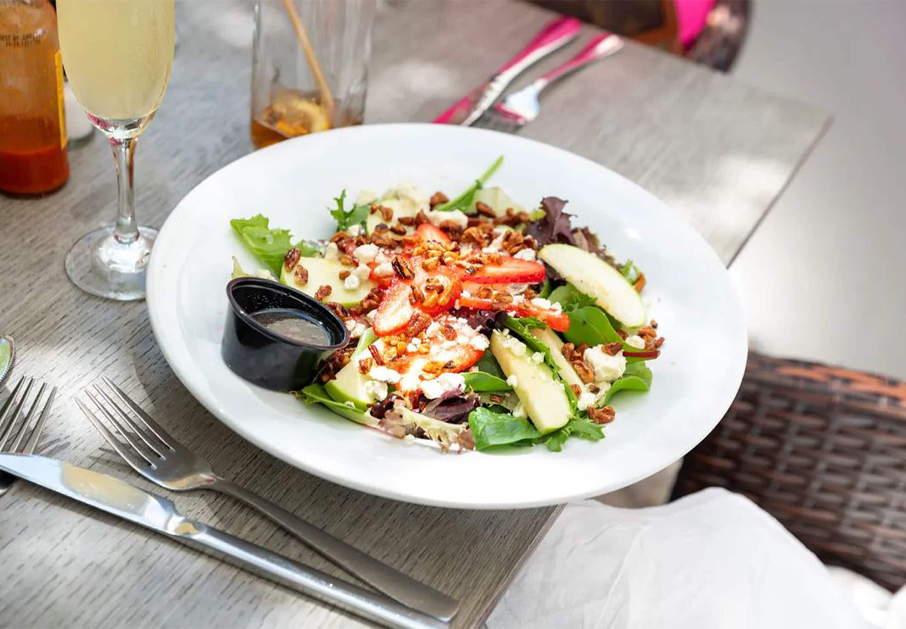 Une assiette de salade garnie de divers ingrédients, accompagnée d’un verre de boisson et de couverts sur une table.