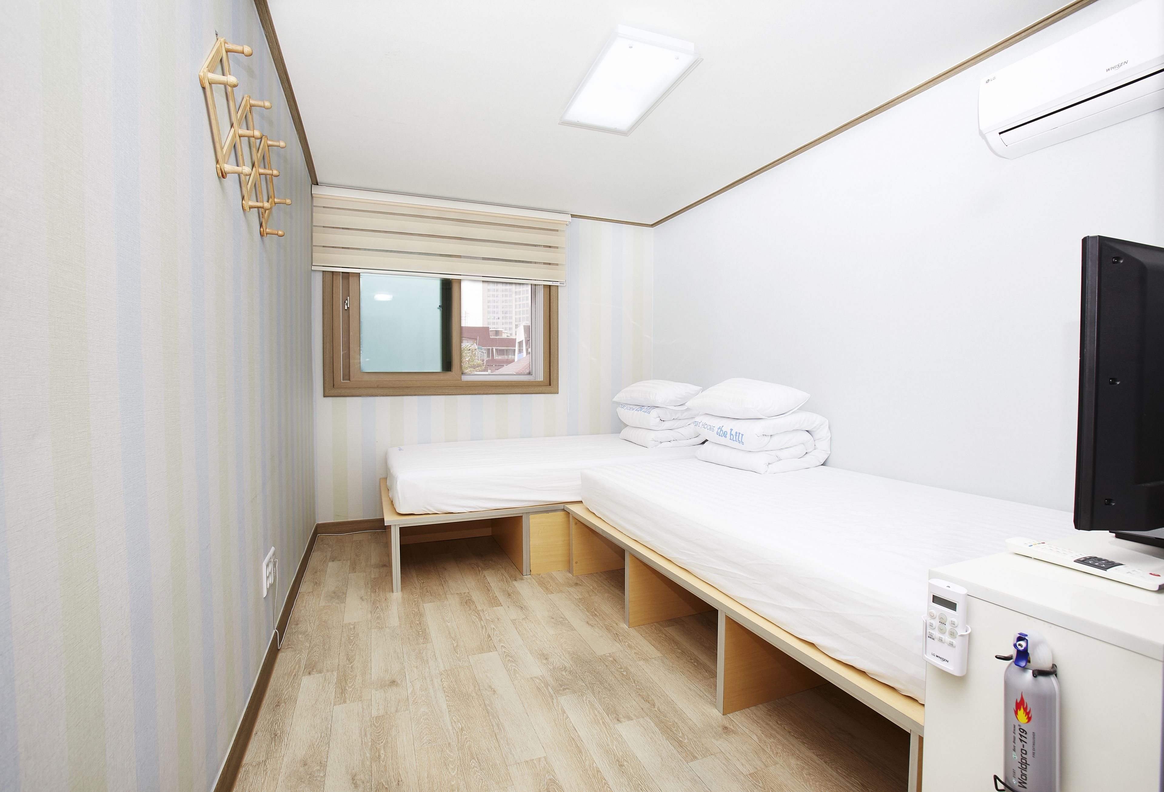 A compact hotel room with a single bed, a small desk with a computer, a window, and a built-in wardrobe.