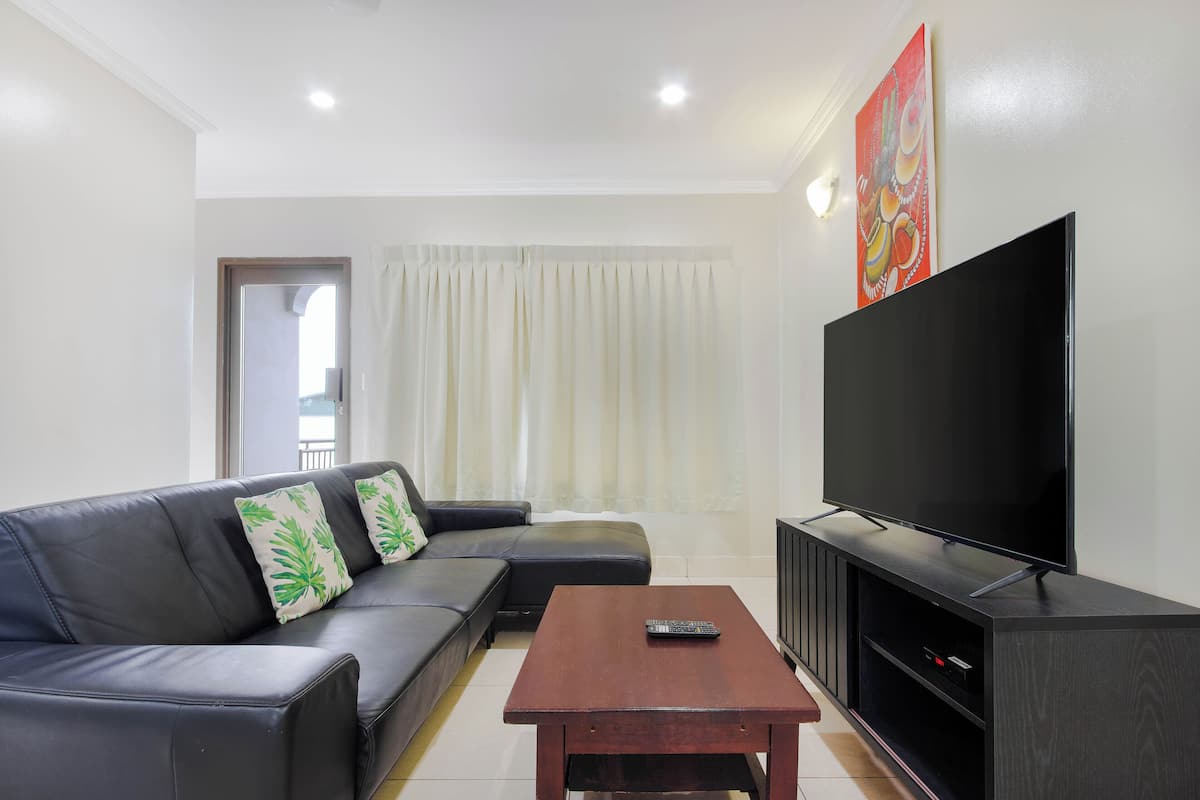 A living room with a black leather sofa, a wooden coffee table, a flat-screen TV, and a painting on the wall.