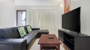 A living room with a black leather sofa, a wooden coffee table, a flat-screen TV, and a painting on the wall.