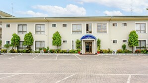 A hotel with a paved parking lot, a central entrance with a blue awning, and symmetrical window placement.