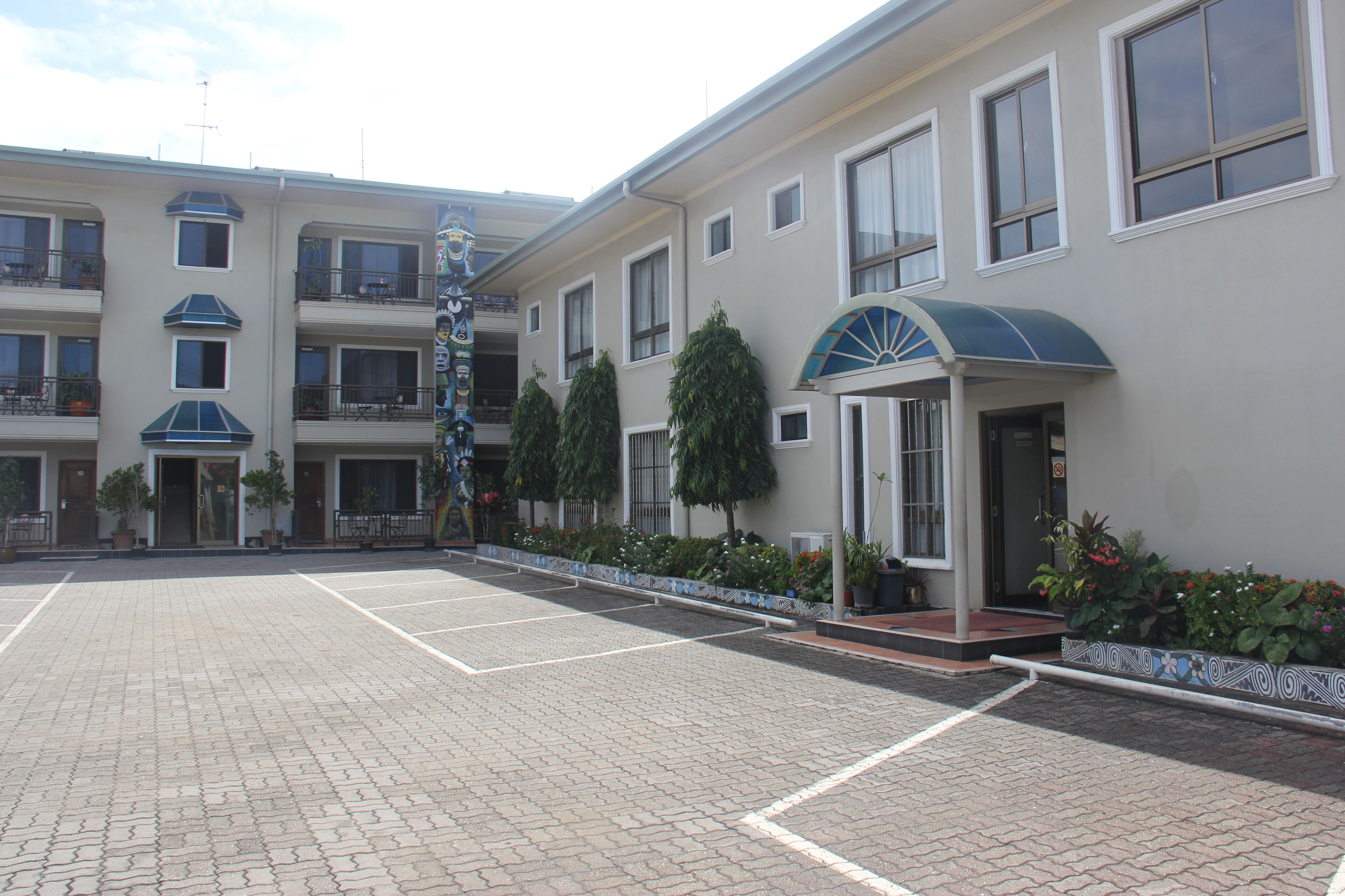 A multi-story hotel with a parking lot, a covered entrance, and potted plants along the walkway.
