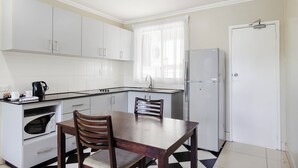 A compact kitchen with white cabinets, a microwave, a refrigerator, and a dining table with chairs.