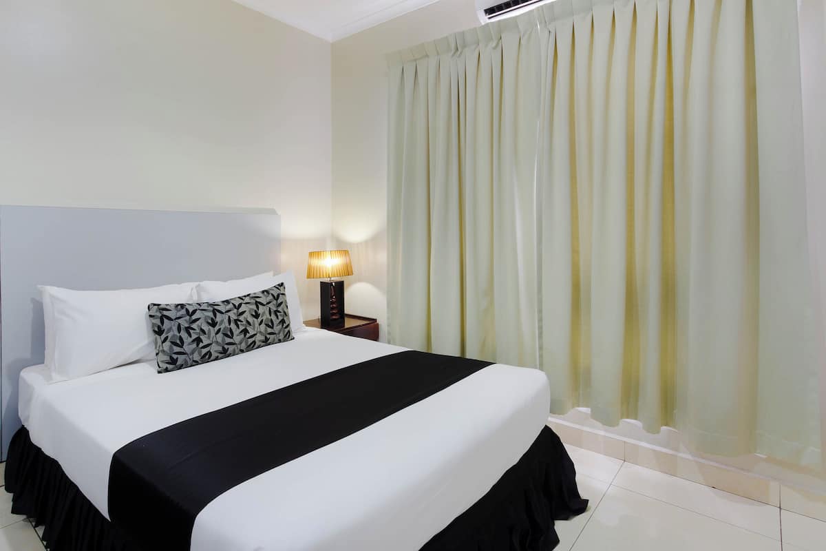 A neatly made bed with white and black bedding, a patterned pillow, and a bedside lamp.