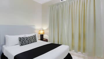Cama bem arrumada com roupa de cama preta e branca, um travesseiro estampado e uma luminária de cabeceira.
