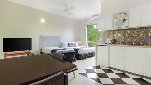 A hotel room with a bed, a desk, a chair, a television, a ceiling fan, and a kitchen area with a microwave and a kettle.