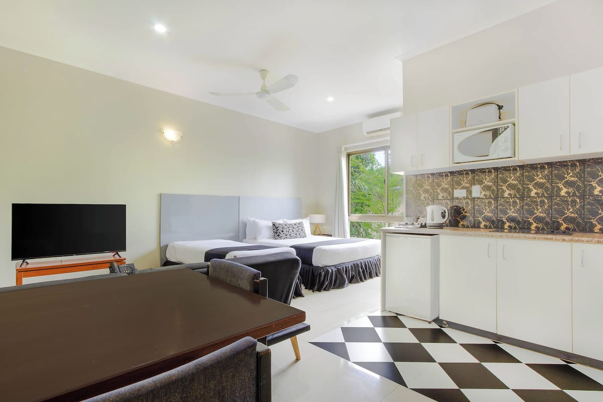 A hotel room with a bed, a desk, a chair, a television, a ceiling fan, and a kitchen area with a microwave and a kettle.