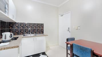 A compact kitchen with white cabinets, a black and gold backsplash, a coffee maker, and a checkered floor.