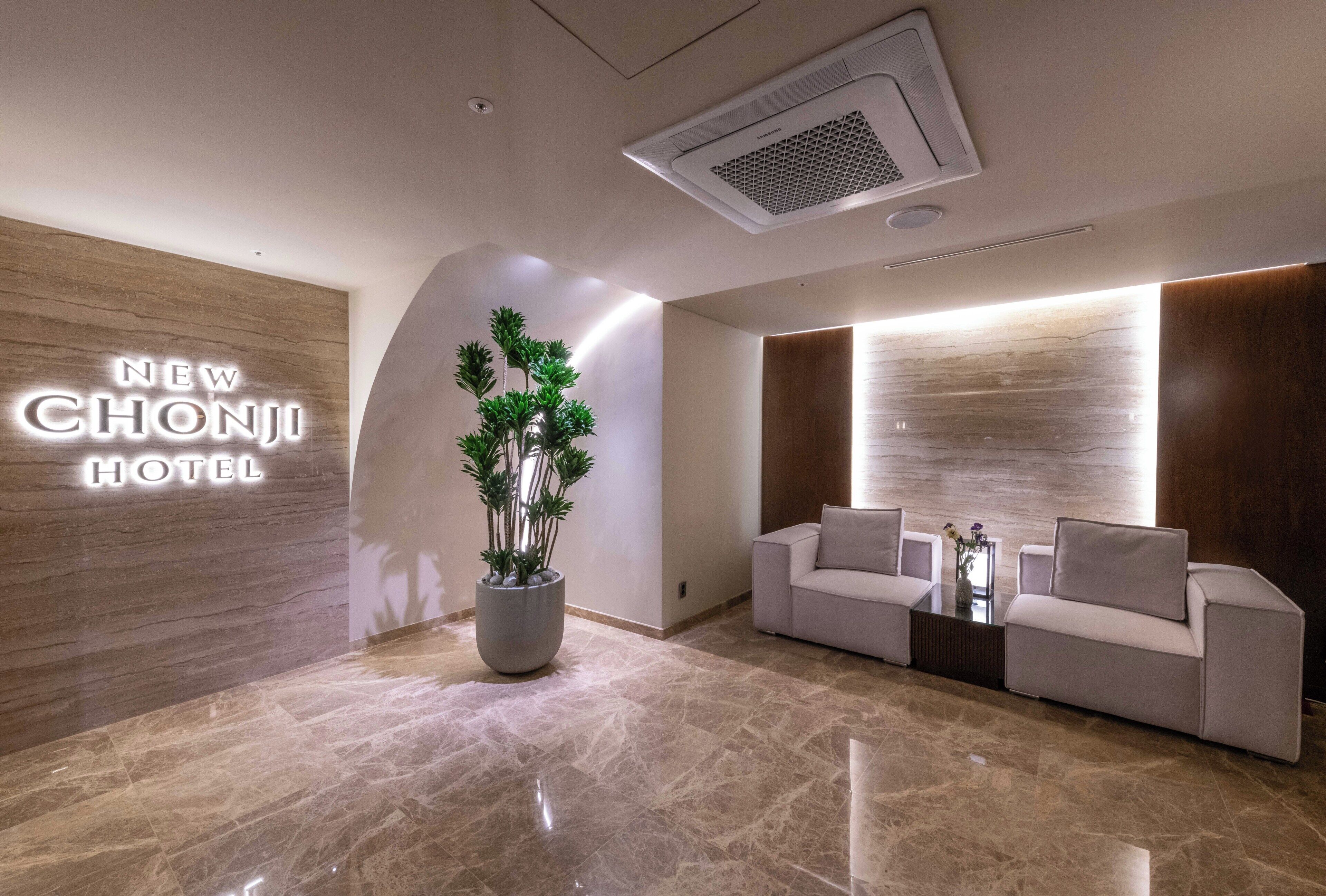 Un moderno vestíbulo de hotel con un mostrador de recepción, una planta grande en maceta y un sofá.
