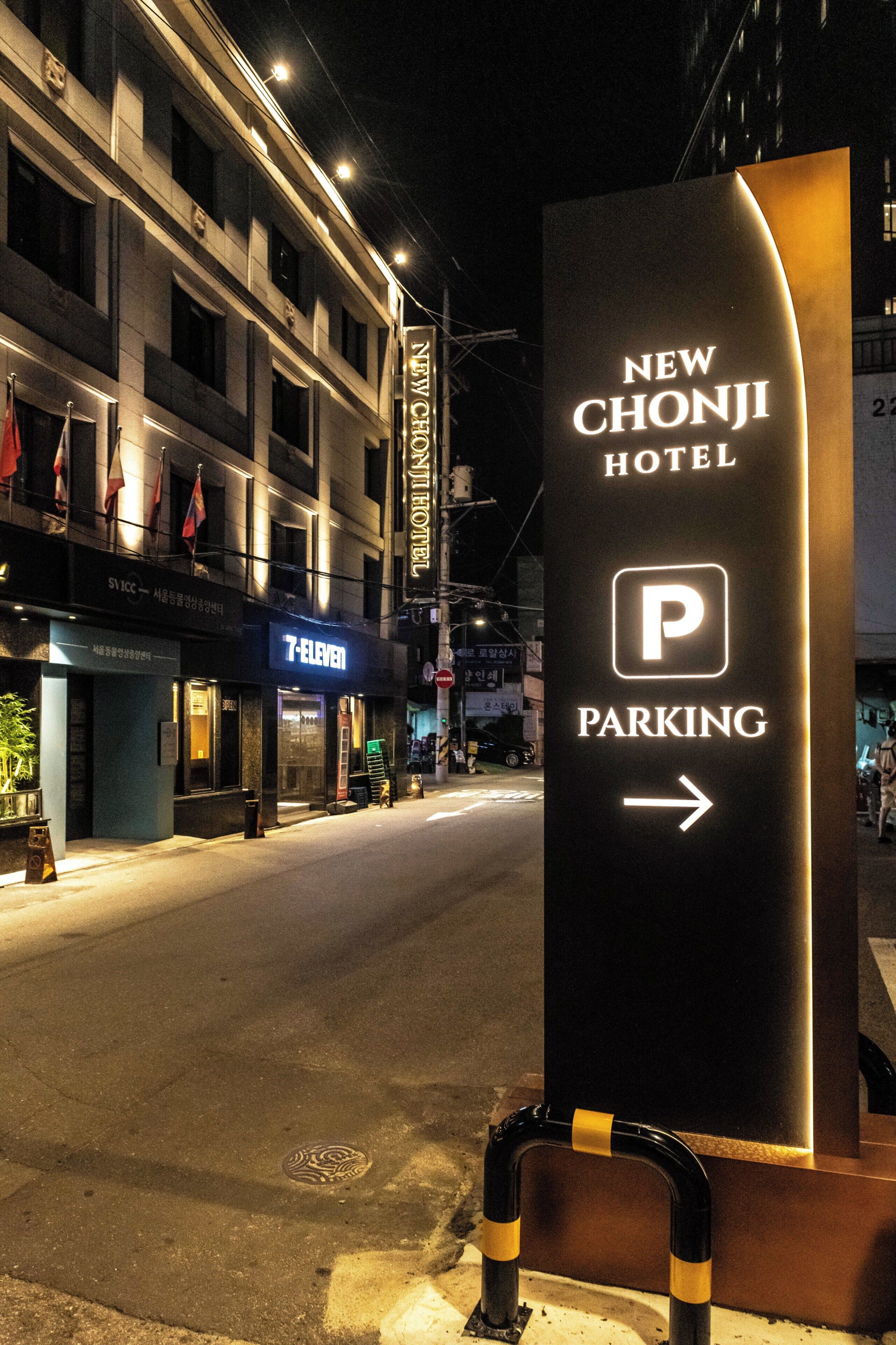 Une vue nocturne d’une rue, avec une enseigne indiquant le New Chonji Hotel et un magasin 7-Eleven.