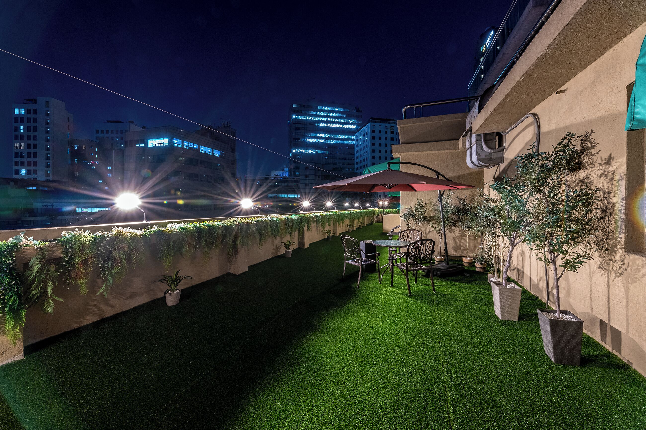 An outdoor terrace with artificial grass, potted plants, and a table with chairs.