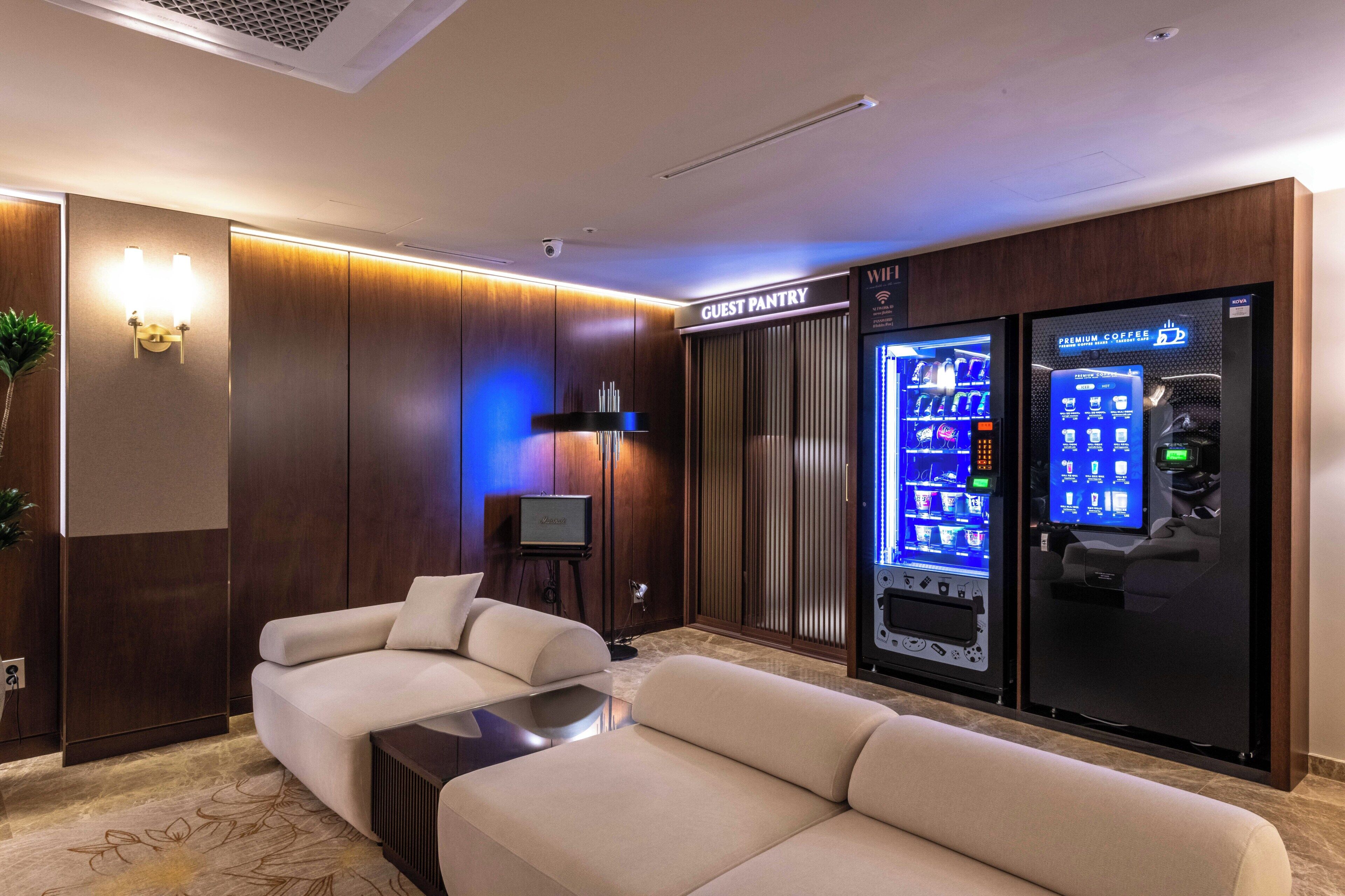 Eine moderne Hotelhalle mit einer Couch, einem Fernseher, einem Getränkeautomaten und einem Schild für die Speisekammer der Gäste.
