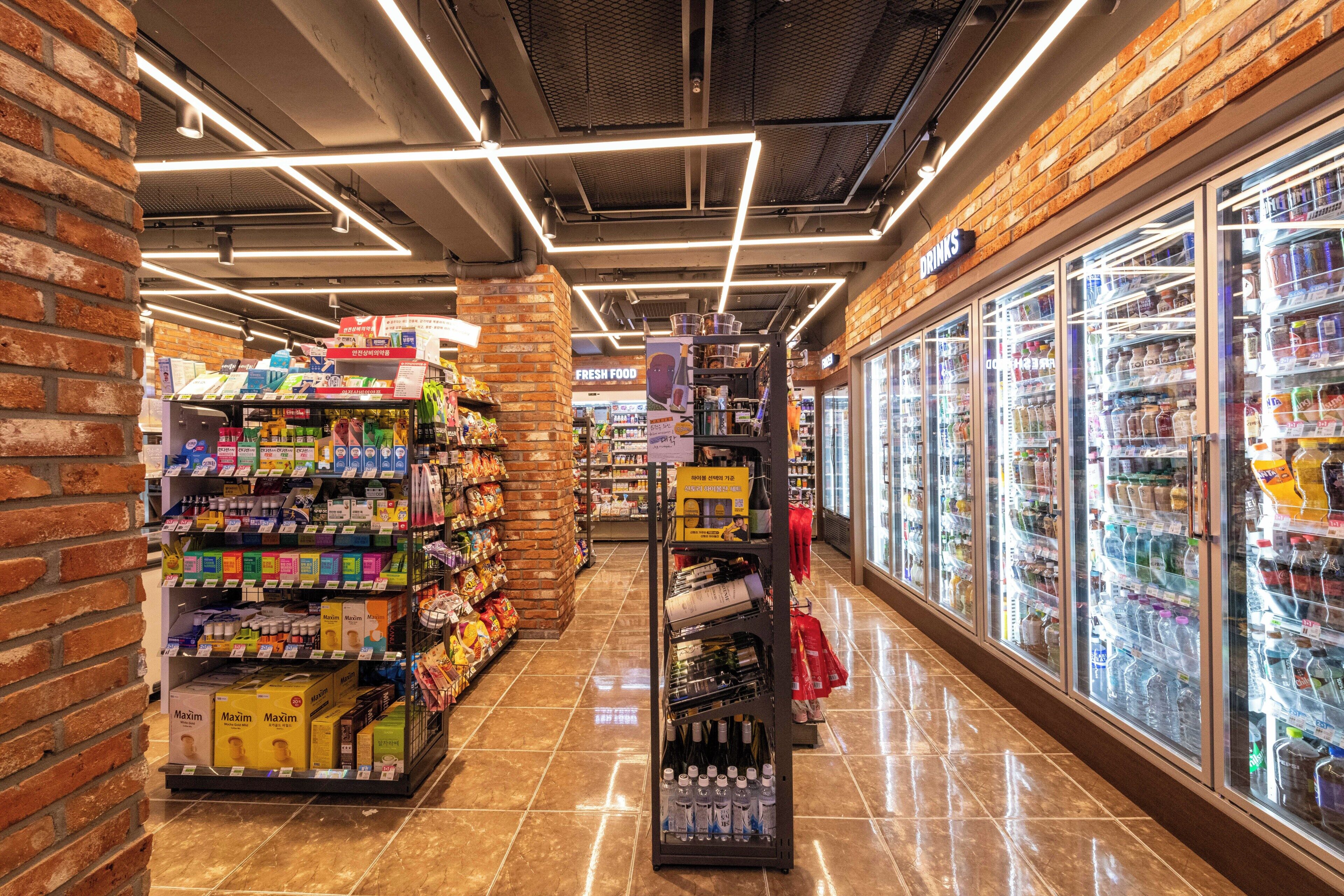 Une épicerie dont les étagères sont remplies de divers produits, avec un rayon réfrigéré et un mur en briques sur l’un des côtés.
