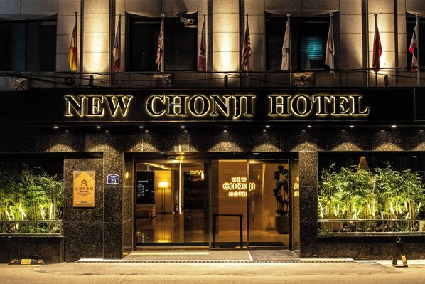 The exterior of the New Chonji Hotel with a prominent entrance, flags, and a well-lit facade.