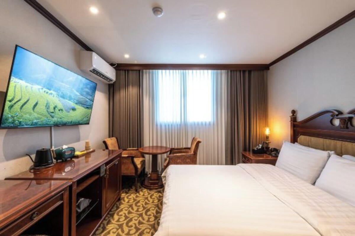 A hotel room with a large bed, a desk with a chair, a television, and a window with curtains.