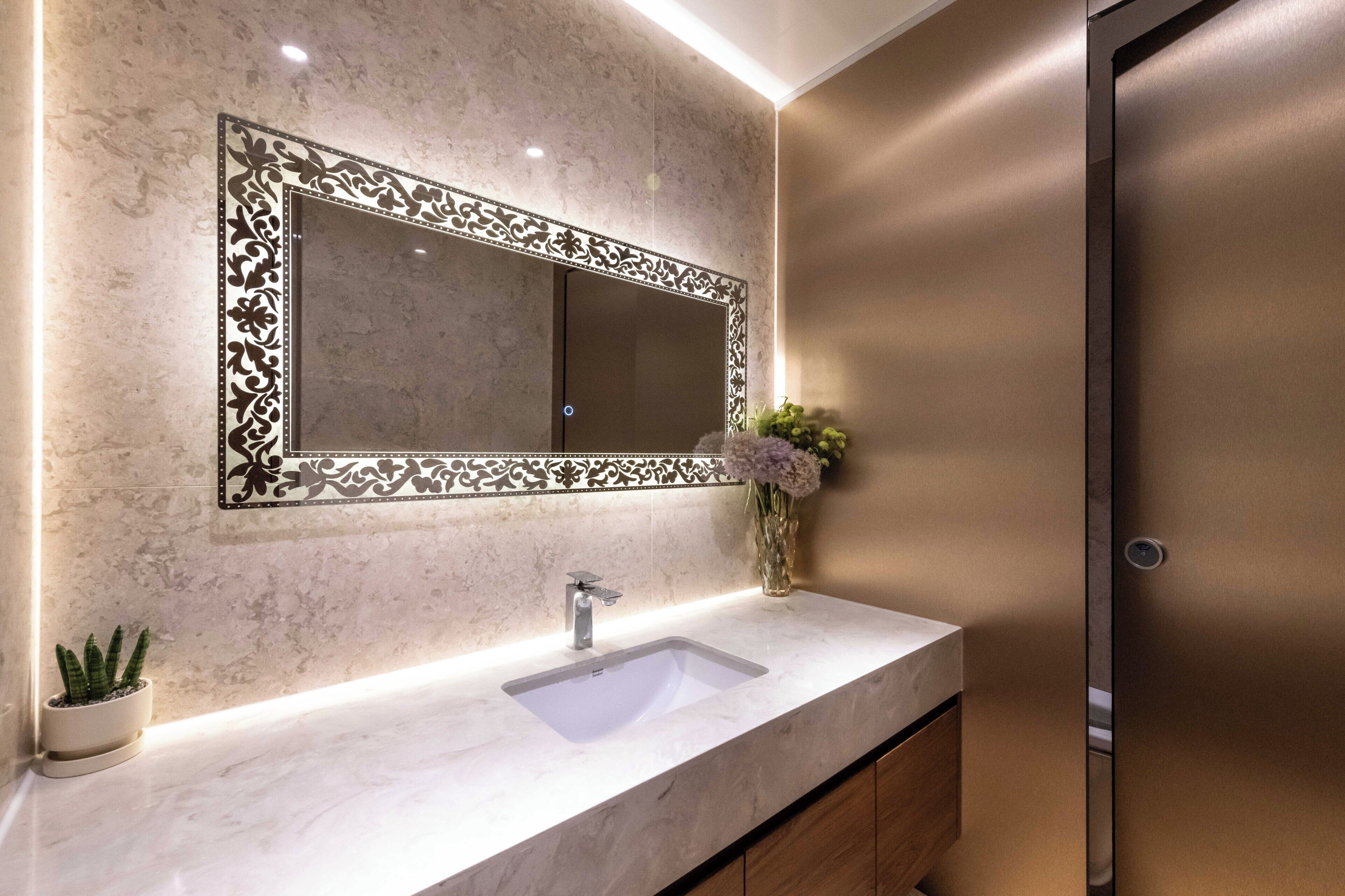 A bathroom with a marble sink, a decorative mirror, and a vase with flowers.