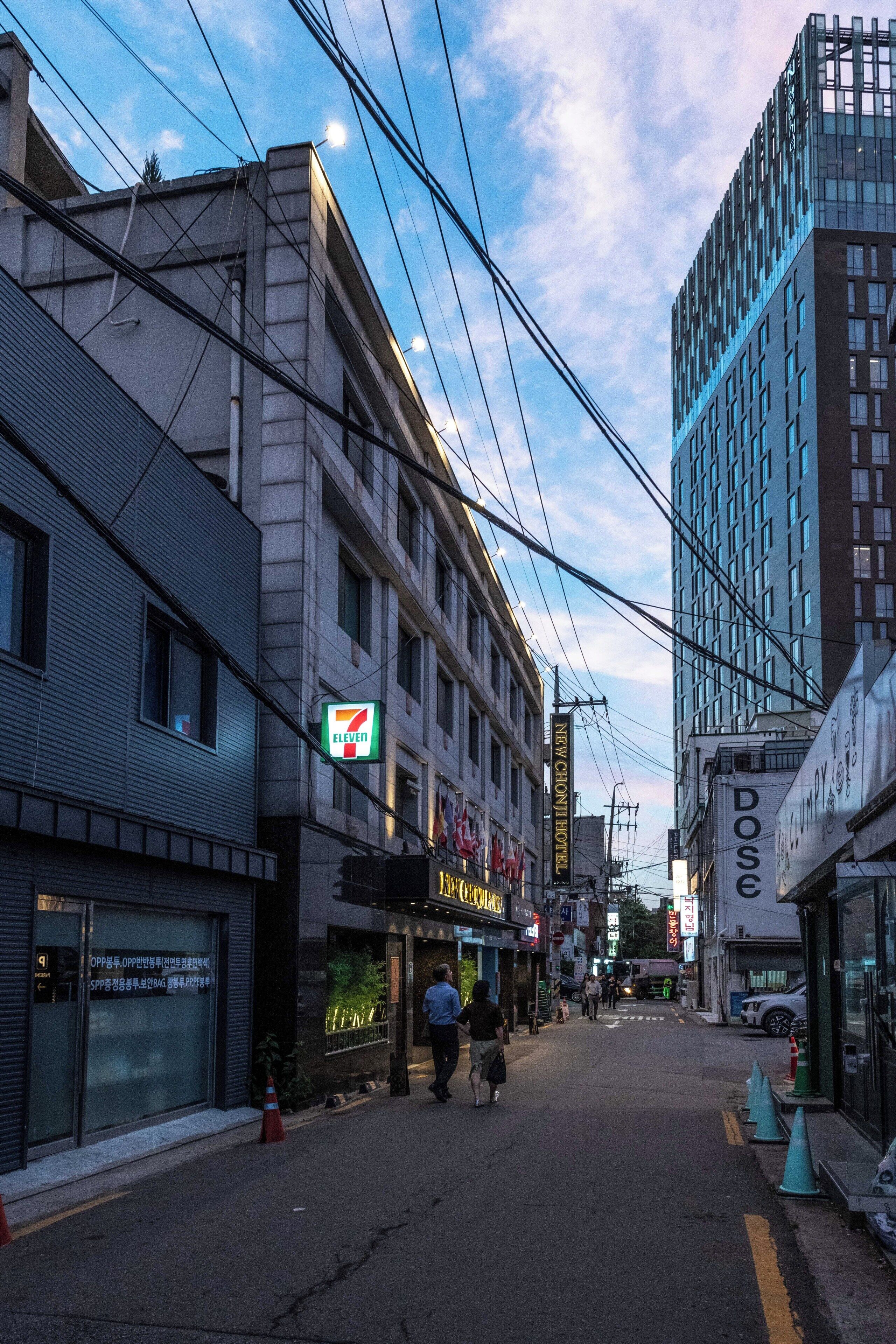 Vista del carrer amb edificis, una botiga 7-Eleven i un cartell d'un hotel Chonchon nou.