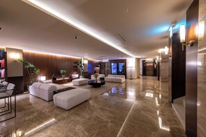 A modern lobby with a seating area, a reception desk, and a digital screen displaying information.