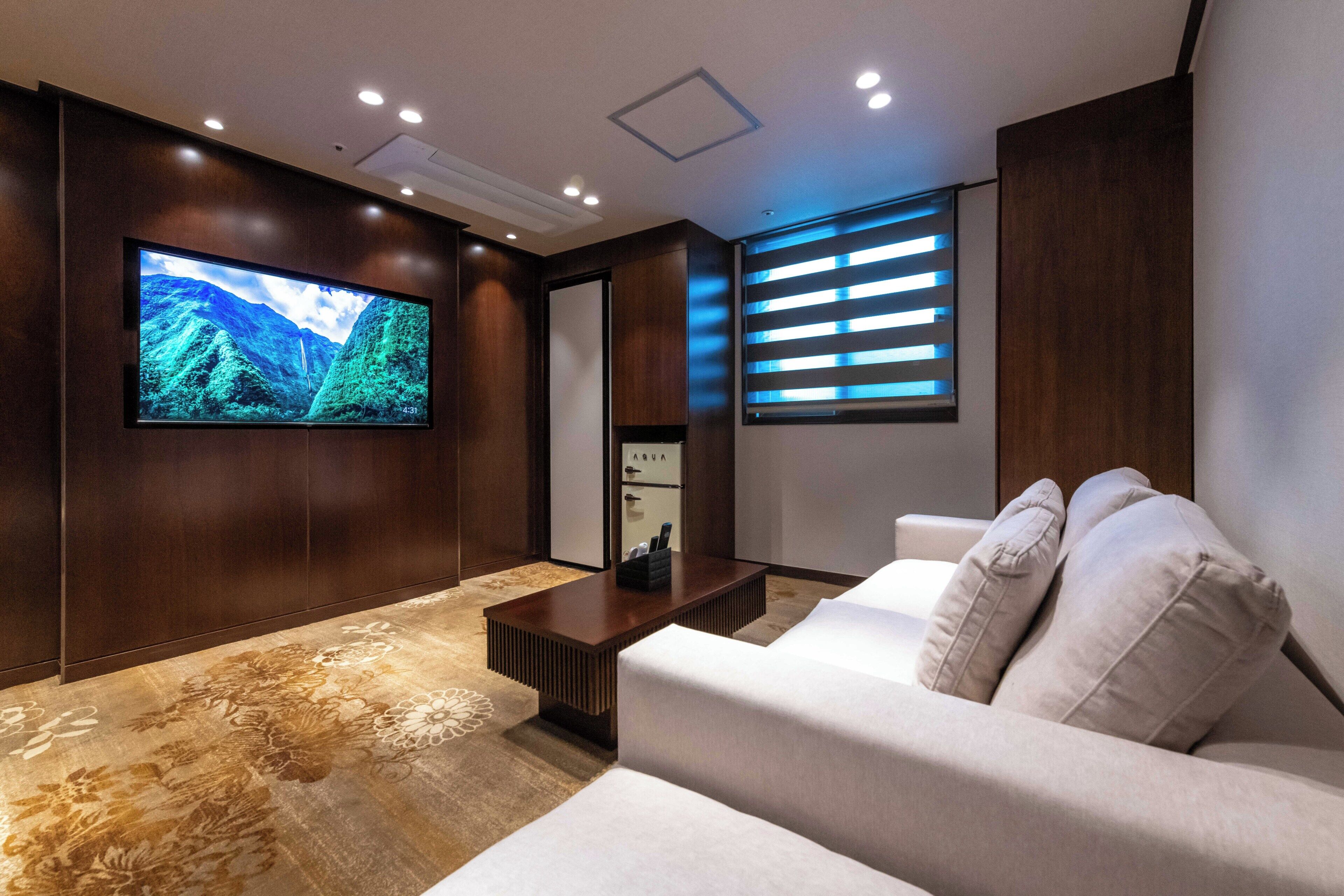 A modern living room with a flat-screen TV, a sofa, a coffee table, and a window with blinds.