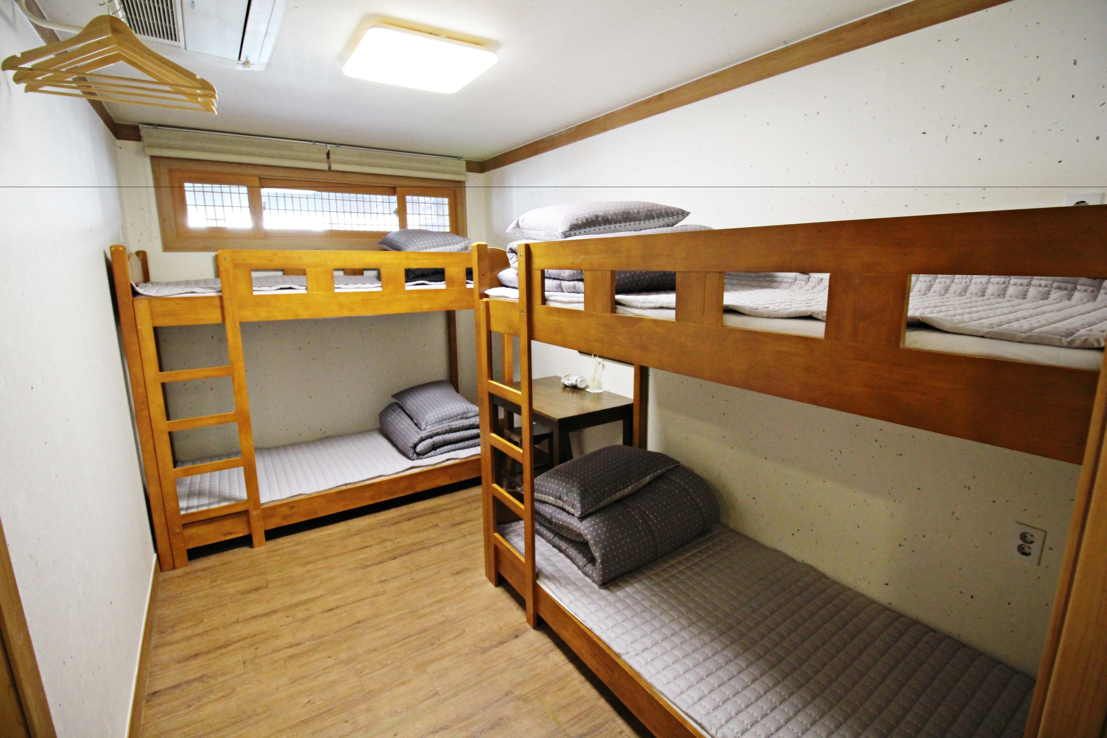 A dormitory room with bunk beds, a window, and a table.