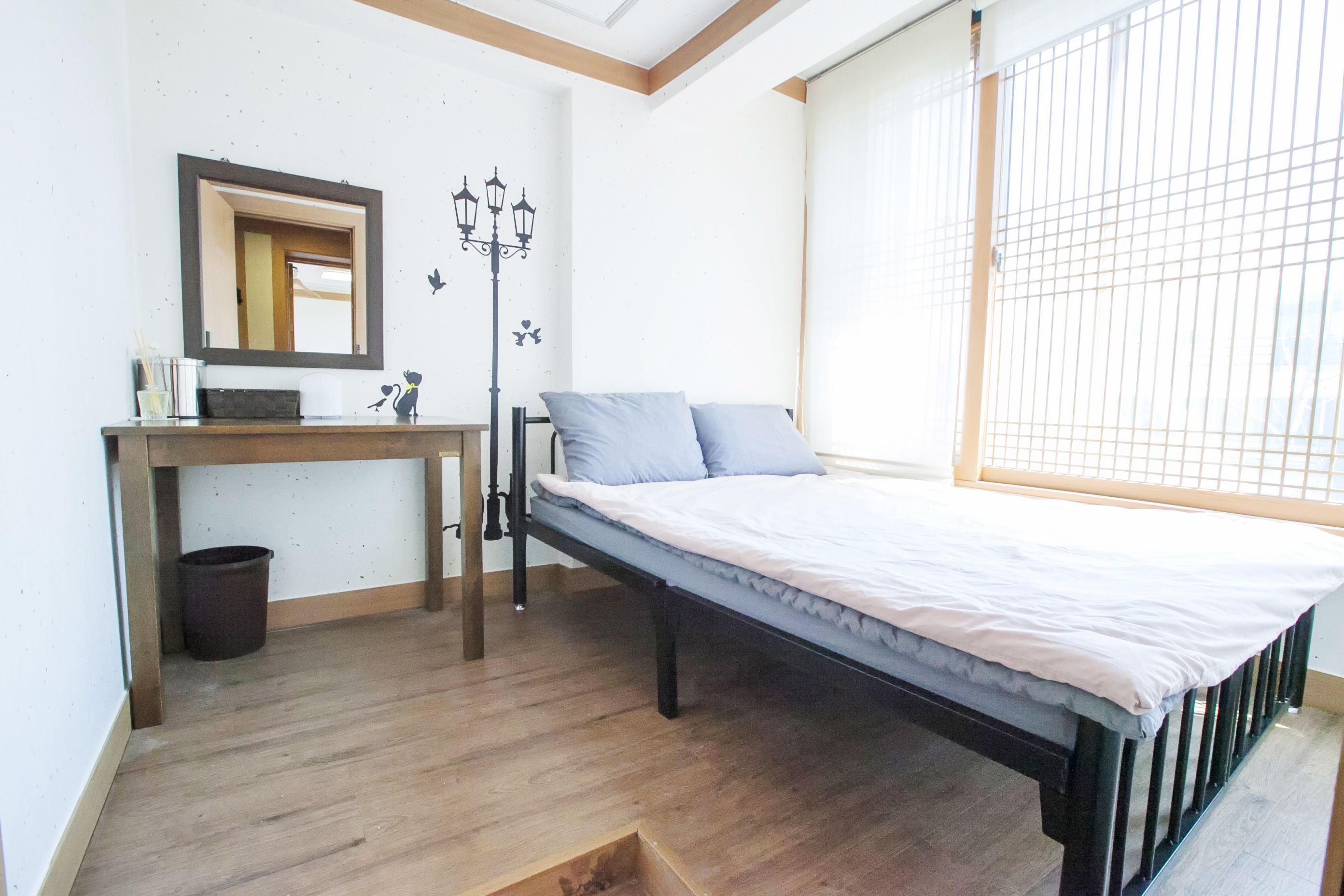A bedroom with a bed, a desk, a mirror, and a window with blinds.