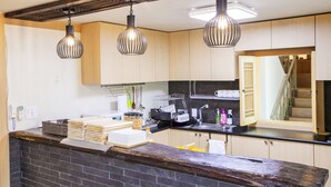 A modern kitchen with wooden cabinets, a black countertop, and three hanging pendant lights. - Cocoa Guesthouse (Seoul)