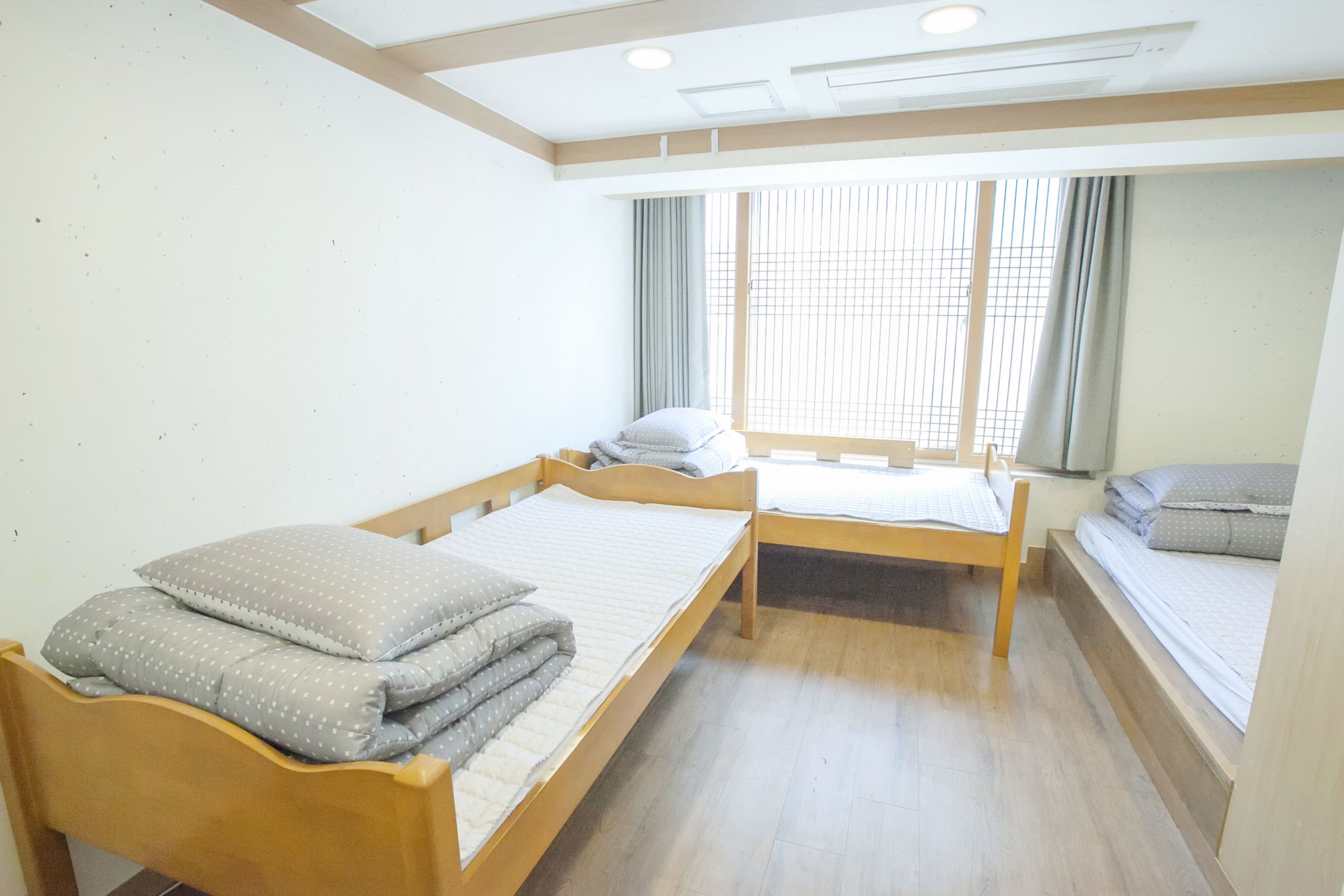 Een hotelkamer met twee houten bedden, een raam met zonwering en een plafond met inbouwverlichting.