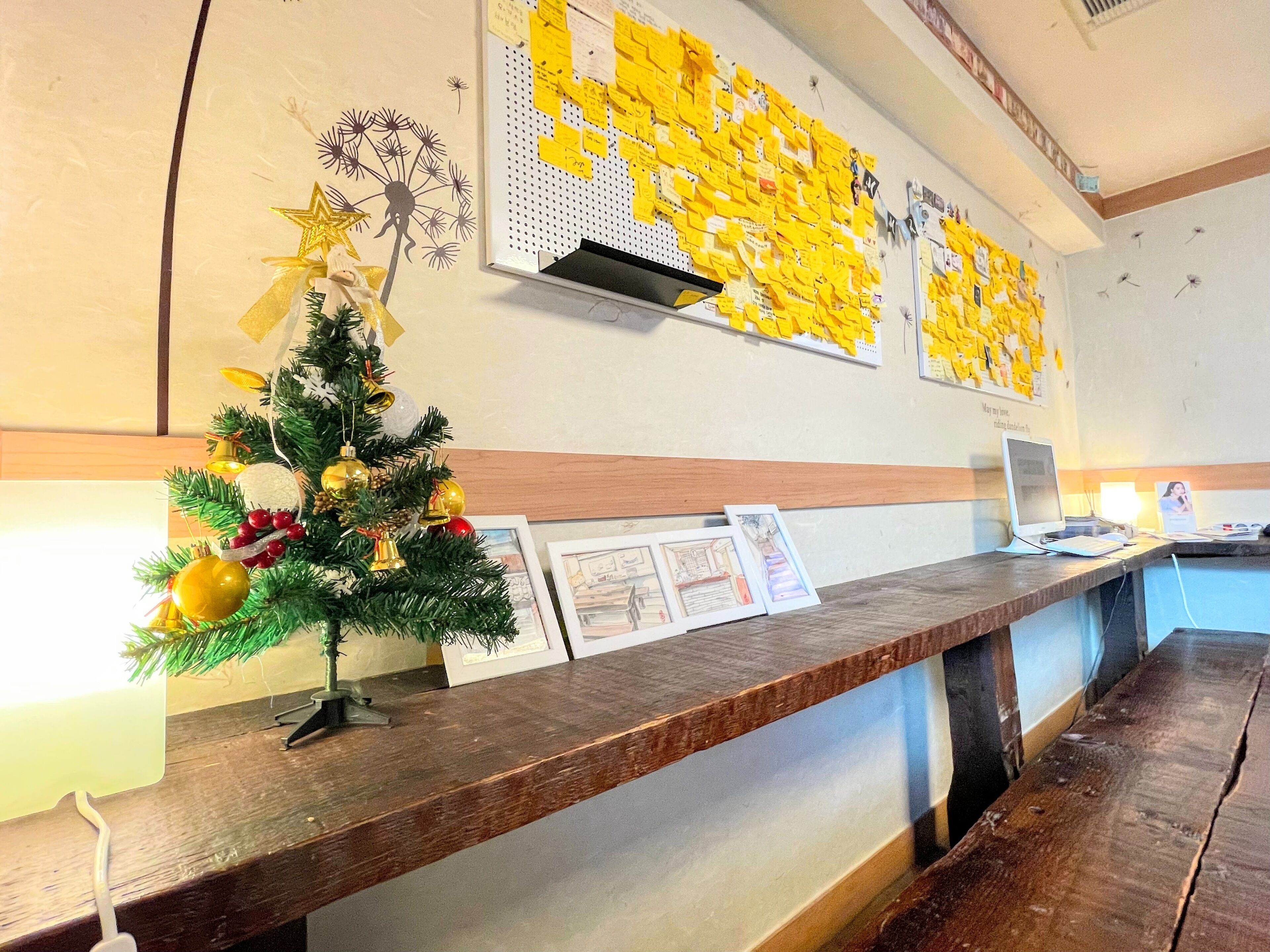 A reception desk with a small Christmas tree, framed pictures, and a wall with yellow notes.