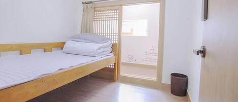 A single bed with a wooden frame and a white mattress, a small trash bin, and a sliding door leading to an outdoor area.