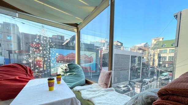 A balcony with a table, cushions, and a view of the cityscape. - Cocoa Guesthouse (Seoul)