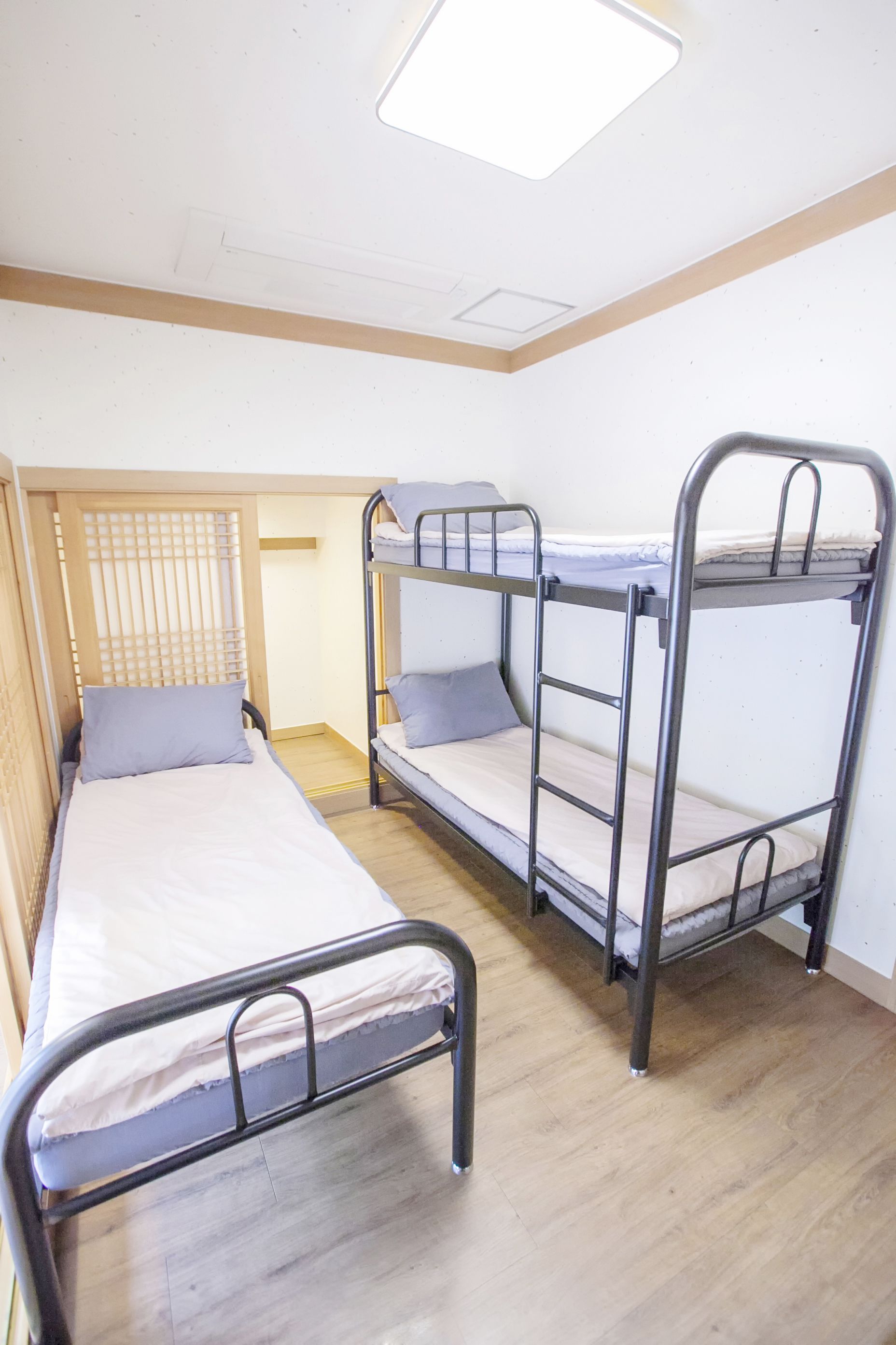 A dormitory room with bunk beds, a wooden floor, and a ceiling light fixture.